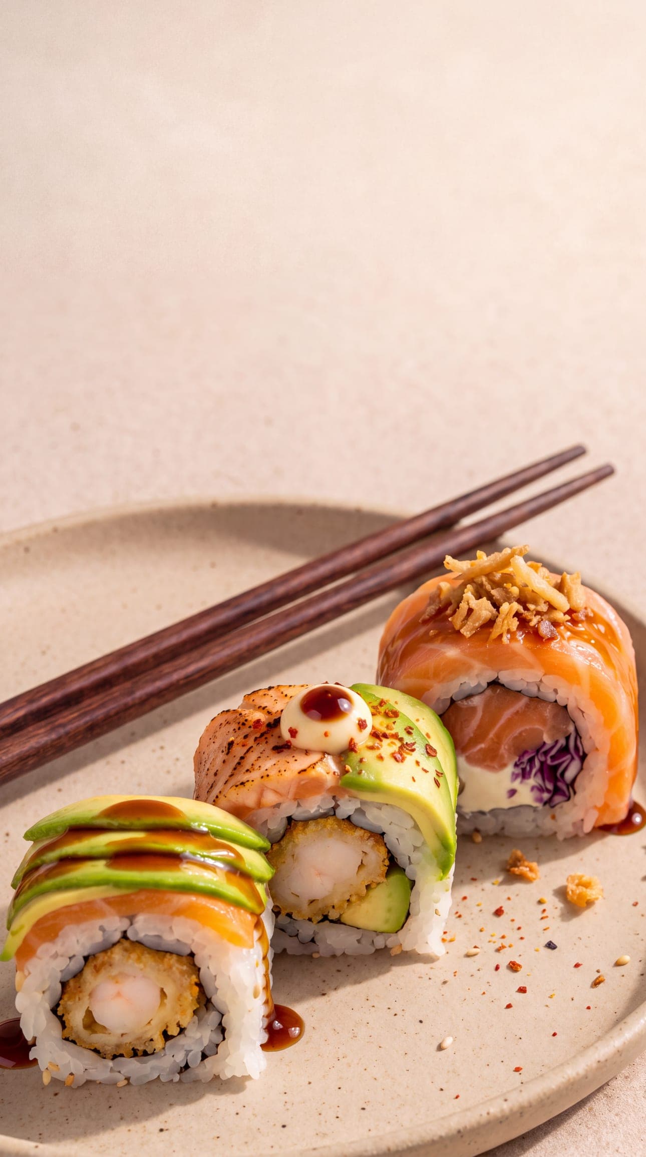 Trois makis KOTTO sur une assiette en grès, saumon, avocat et crevette tempura, avec des baguettes en bois.